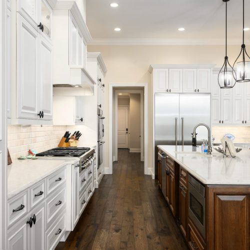 Bright and spacious kitchen featuring white cabinetry, a large dark wood island, stainless steel appliances, and pendant lighting, perfect for family cooking and entertaining.