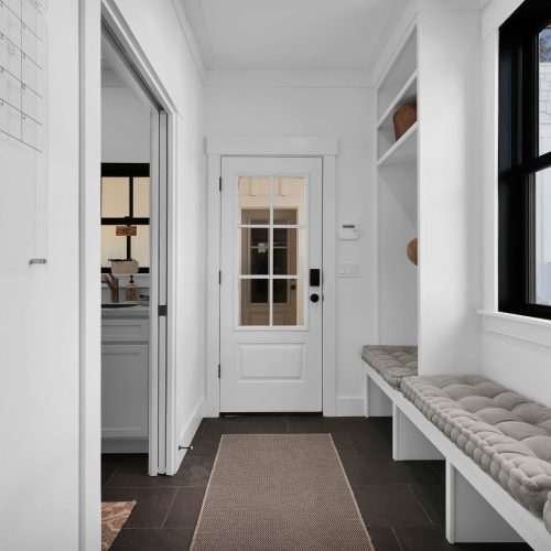 Bright and welcoming entryway featuring a built-in bench, large windows, and a white door with glass panels, creating an inviting atmosphere for residents and guests.