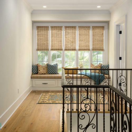 Bright interior with a cozy window seat featuring cushions and bamboo shades, overlooking a lush outdoor view.