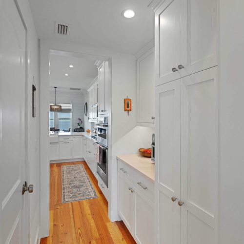 Bright and modern white kitchen with wooden flooring, cabinetry, and stainless steel appliances, featuring a cozy and functional space for cooking and dining.