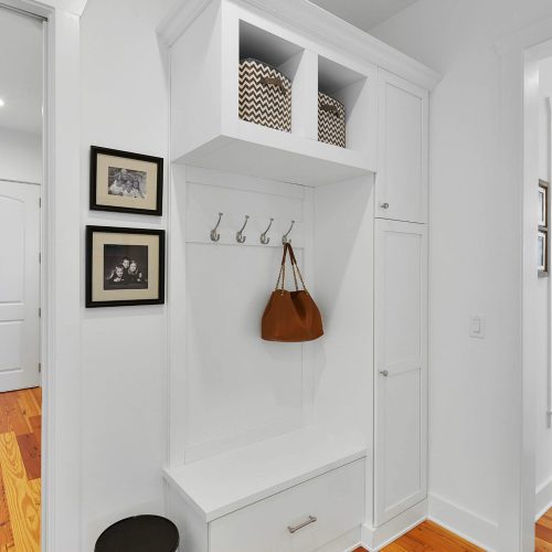 Bright and clean entryway featuring a built-in storage bench, hooks for coats, and decorative wall art, creating an inviting space in a contemporary home.