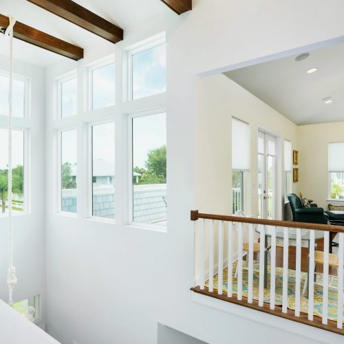 Sunlit living room featuring expansive windows that bring in natural light, high ceilings with wooden beams, and a cozy seating area with a TV and decorative accents.