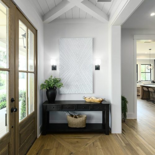 Elegant entryway featuring a wooden door, a black console table, and contemporary wall art in a bright, open home interior.