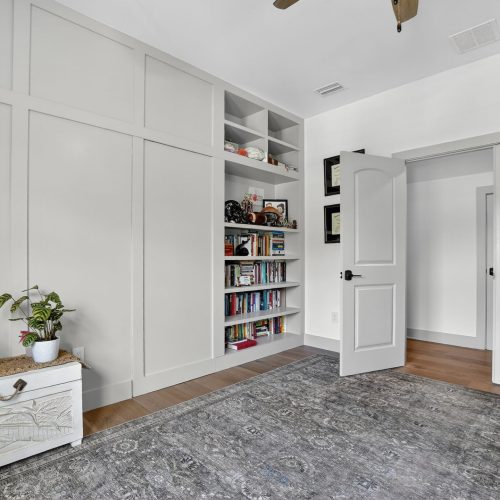 Bright, modern interior room with white walls, built-in bookshelves, and a door, featuring a cozy rug and decorative plants.