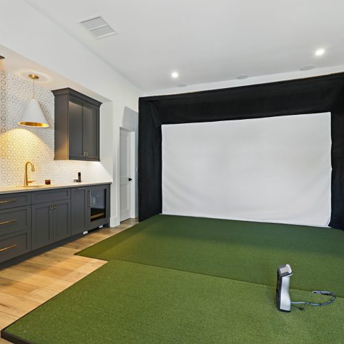 Interior view of a home theater room featuring a large projection screen, green carpet, and modern kitchen cabinets in the background.