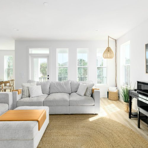 A spacious, contemporary living room featuring large windows that fill the space with natural sunlight, comfortable gray sofas, and stylish decor, creating an inviting atmosphere.