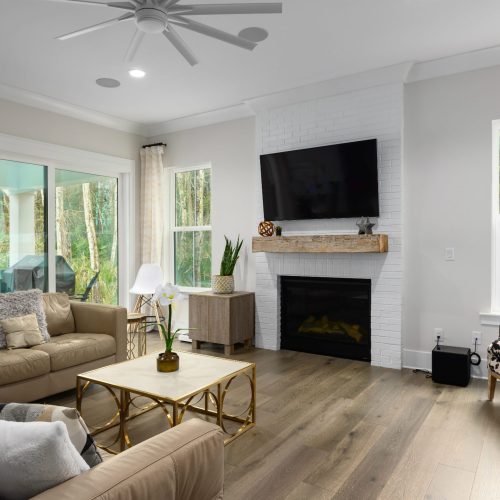 Bright and airy living room featuring a white brick fireplace, wall-mounted TV, and comfortable seating with neutral tones.