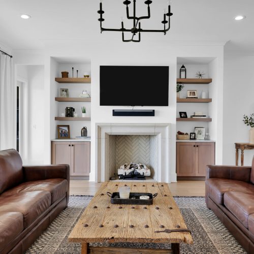Bright living room featuring a fireplace, wall-mounted TV, and built-in shelves filled with decorative items and books.