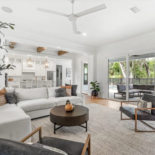 Spacious living room featuring a white sectional sofa, contemporary armchairs, and large sliding glass doors that open to a backyard pool area. Bright, airy, and perfect for relaxing or entertaining.