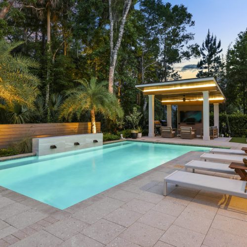 Luxurious outdoor swimming pool surrounded by lush greenery and palm trees, featuring a shaded cabana and comfortable lounge chairs for relaxing evenings.