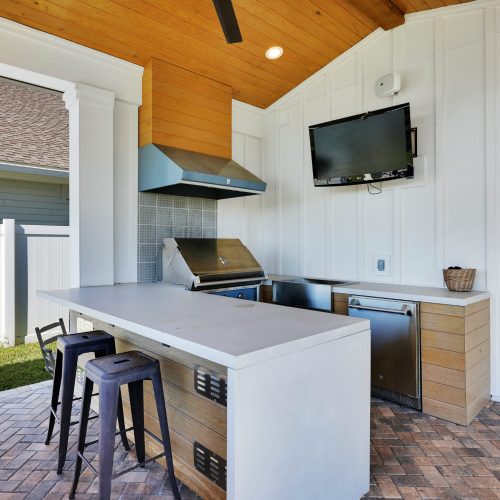 Outdoor kitchen featuring a built-in grill, countertop, and mounted TV in a contemporary backyard setting.