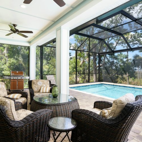 A spacious outdoor living space featuring a screened enclosure, comfortable wicker furniture, and a swimming pool, perfect for relaxing and entertaining in a private backyard setting.