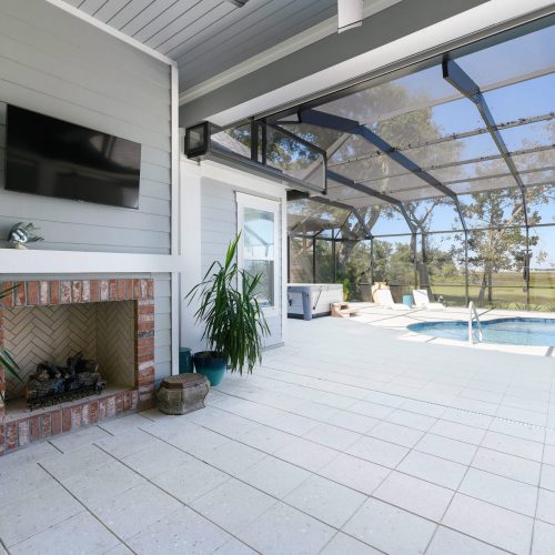 Outdoor screened pool area with fireplace and mounted TV for relaxing and entertaining.