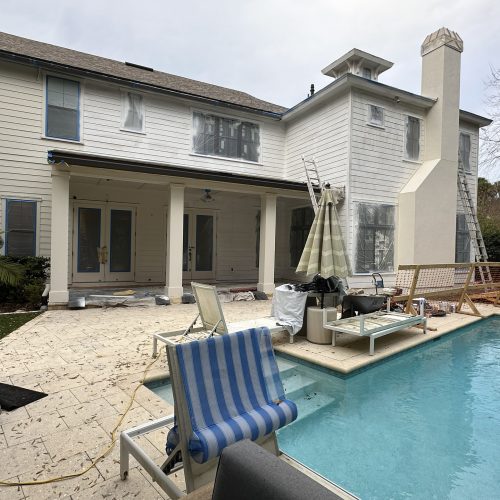 Modern two-story house under renovation with plastic-covered windows and construction materials around a swimming pool in a backyard.