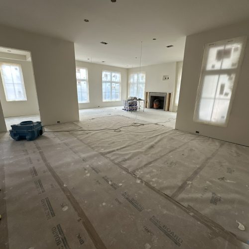 Spacious living room under construction with large windows, neutral walls, and an unfinished fireplace, showcasing modern interior design and upcoming home finishes.