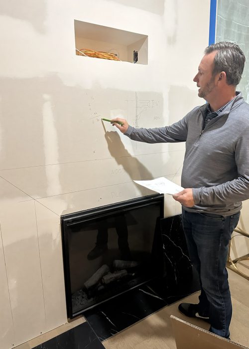 1. Interior construction site with a man analyzing sketches on drywall near a fireplace, showing residential building progress.