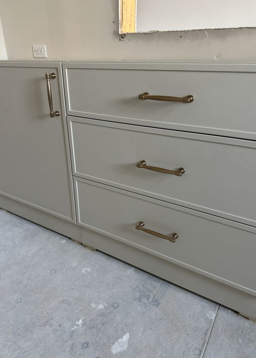Bright white kitchen cabinet with sleek metal handles, under construction, neutral background, showcasing modern cabinetry design.