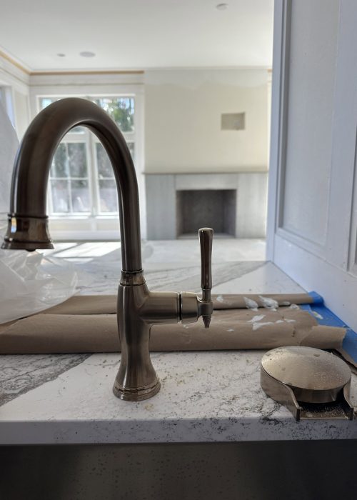 Elegant stainless steel kitchen faucet installed on a marble countertop with construction tools nearby.