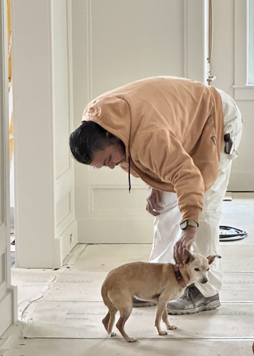 Renovation worker gently petting a small dog inside a house during a home improvement project.