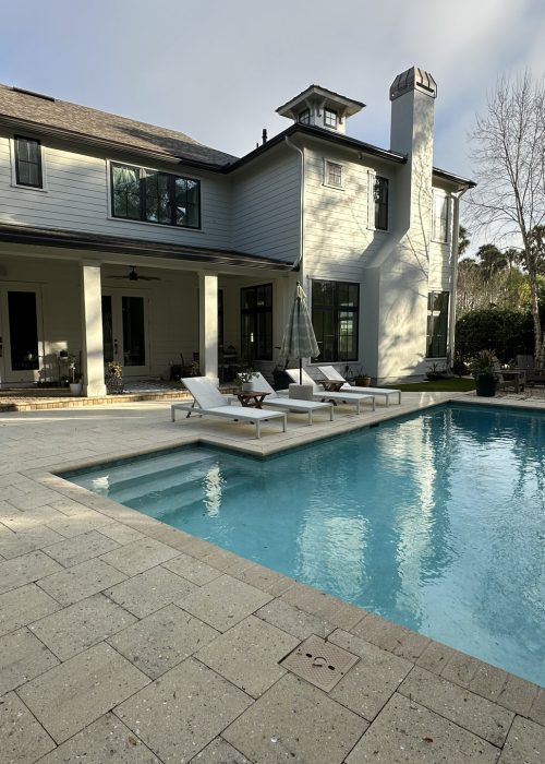 A luxurious two-story house featuring a backyard pool, outdoor seating area, and lush landscaping, perfect for relaxing and entertaining.