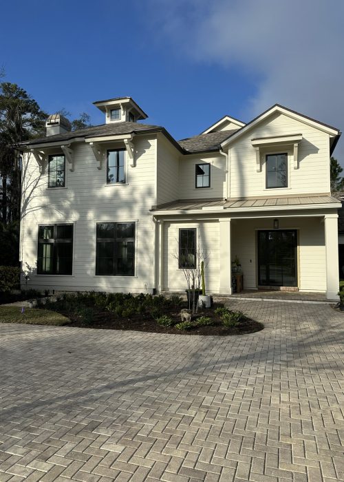 A spacious home featuring multiple gables, large windows, and a welcoming front porch, set against a bright blue sky with lush greenery.