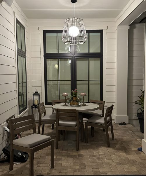 Bright dining room featuring large windows, a round table with six chairs, and a stylish chandelier, creating a welcoming space for family meals and gatherings.