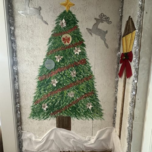 Colorful Christmas tree wall decoration with ornaments, surrounded by reindeer and a gift box, enhanced with tinsel and festive decor for holiday cheer.