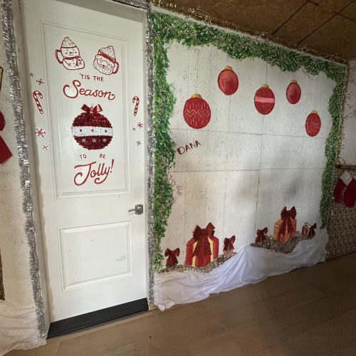 Festive holiday door decoration featuring seasonal ornaments, red bows, stockings, and personalized touches for Christmas cheer.