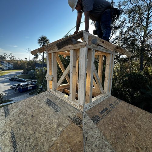 1. A construction worker installing a wooden structure on a roof, wearing a safety helmet and working during daylight.