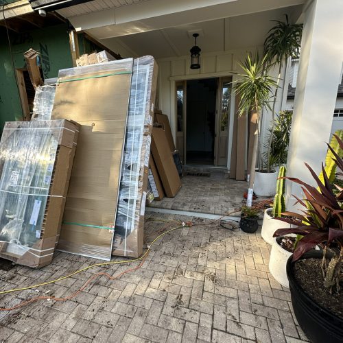 Newly built house with construction materials and plants at the entrance, showcasing modern architecture and landscaping details.