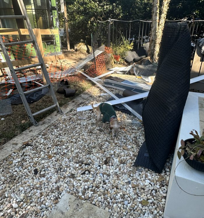 1. Construction site with tools, materials, and a small dog on gravel, showing ongoing building or remodeling work outdoors.
