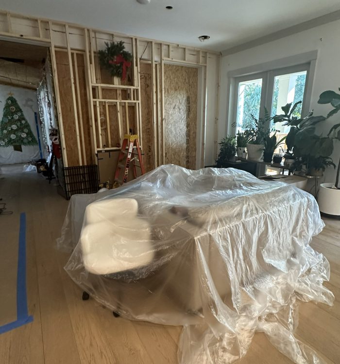 1. An interior view of a house under renovation, featuring exposed wall framing with Christmas decorations, a construction ladder, and a covered table on a hardwood floor.