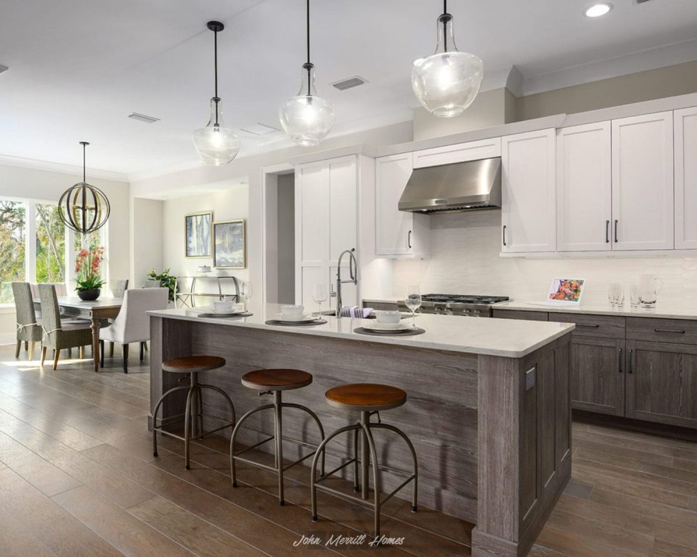 Modern open-concept kitchen with white cabinetry, stainless steel appliances, and a large island with seating, featuring pendant lighting and a view into the adjacent dining and living areas.
