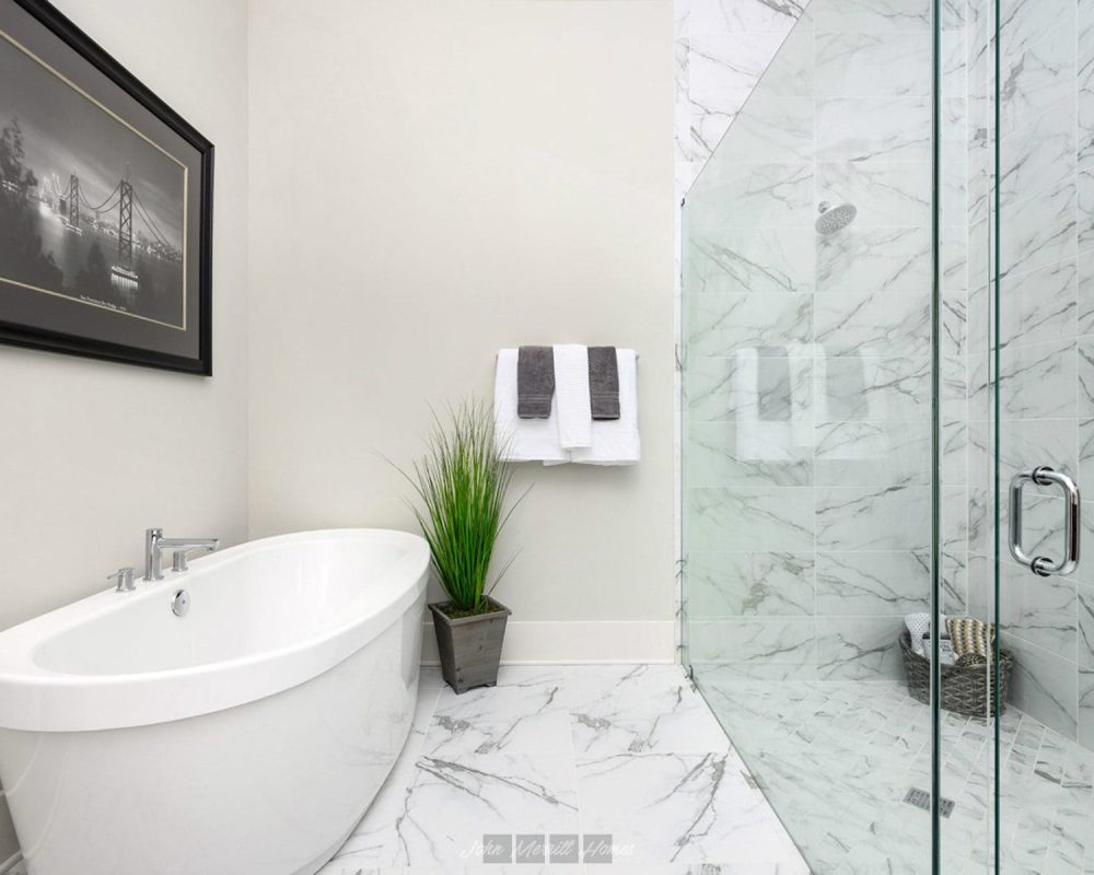 Luxurious modern bathroom featuring a sleek white soaking tub, a marble-tiled shower with glass enclosure, and elegant decor including a framed artwork, a potted plant, and neatly hung towels.