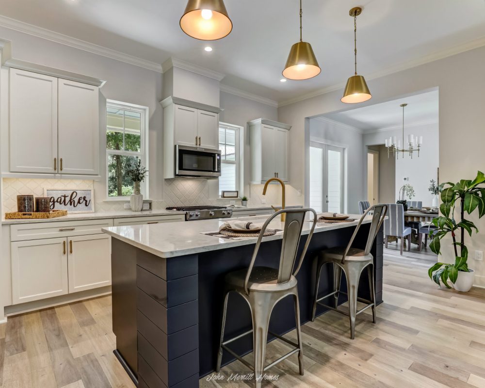 Modern kitchen with white cabinets, a navy blue island, stainless steel appliances, and pendant lighting, showcasing contemporary design and open-concept living.