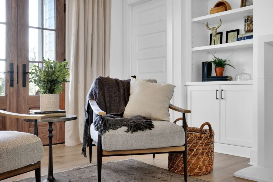 A welcoming living room featuring a comfortable armchair with pillows, a side table with a potted plant, and built-in white shelves with decorative items, creating a warm and inviting atmosphere.