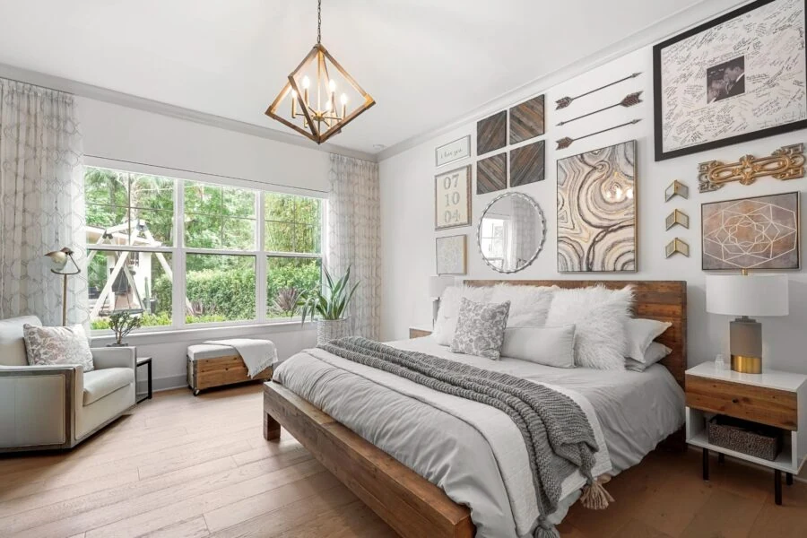 A cozy, well-decorated bedroom featuring a large bed, gallery wall art, and ample sunlight streaming through a big window.