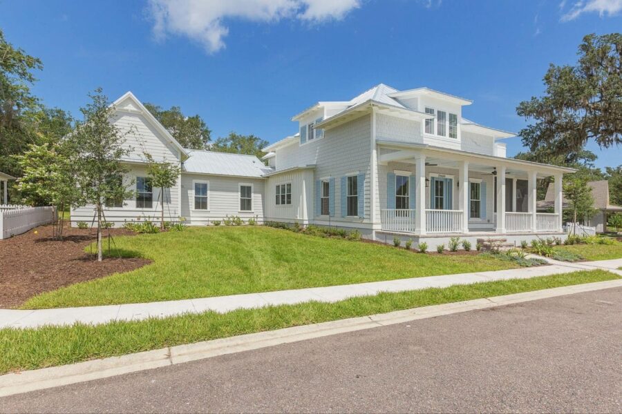 A large, elegant white house with a wrap-around porch, multiple gables, and lush green landscaping, showcasing a beautiful residential property.