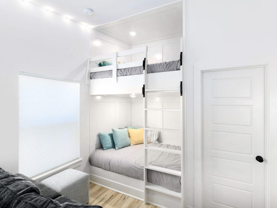 Bright white bedroom with bunk beds, cozy seating area, and modern interior design, featuring a compact space with efficient use of all available space, perfect for family living.
