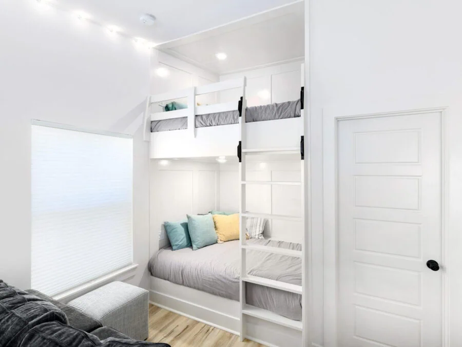 Bright white bedroom with bunk beds, cozy seating area, and modern interior design, featuring a compact space with efficient use of all available space, perfect for family living.