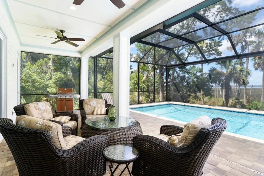 Bright screened-in porch with outdoor seating, a pool, and lush tropical scenery at John Merrill Homes.