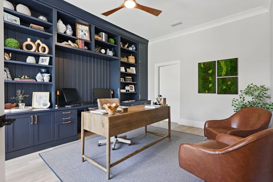 Spacious home office featuring navy blue built-in shelves filled with decorative items, a wooden desk, and comfortable leather chairs, creating an inviting workspace.